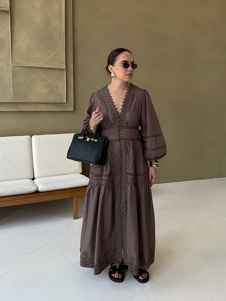 Woman in a brown dress holding a black handbag indoors.